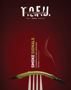 Image contains a dark red background with a silver fork coming up from the bottom of the frame. On the fork, a single piece of asparagus is visible. Both ends of the asparagus are burnt, and the right end has a small stream of smoke coming from it. Above the fork and the asparagus, there are two vertical blocks of text. The larger one on the left says "Smoke Signals". The word "smoke" is in white, and the word "signals" is in green. The smaller block of text says "Is burning out and fading away" in one line and "helping the animals" in another. The words "the animals" are in green. At the very top of the image, there is text that says "T.O.F.U." in white, and within that text there is more text that says "T.O.F.U. Magazine". Just below the white T.O.F.U., there is text that says "Issue 14 Burnout March 2019".